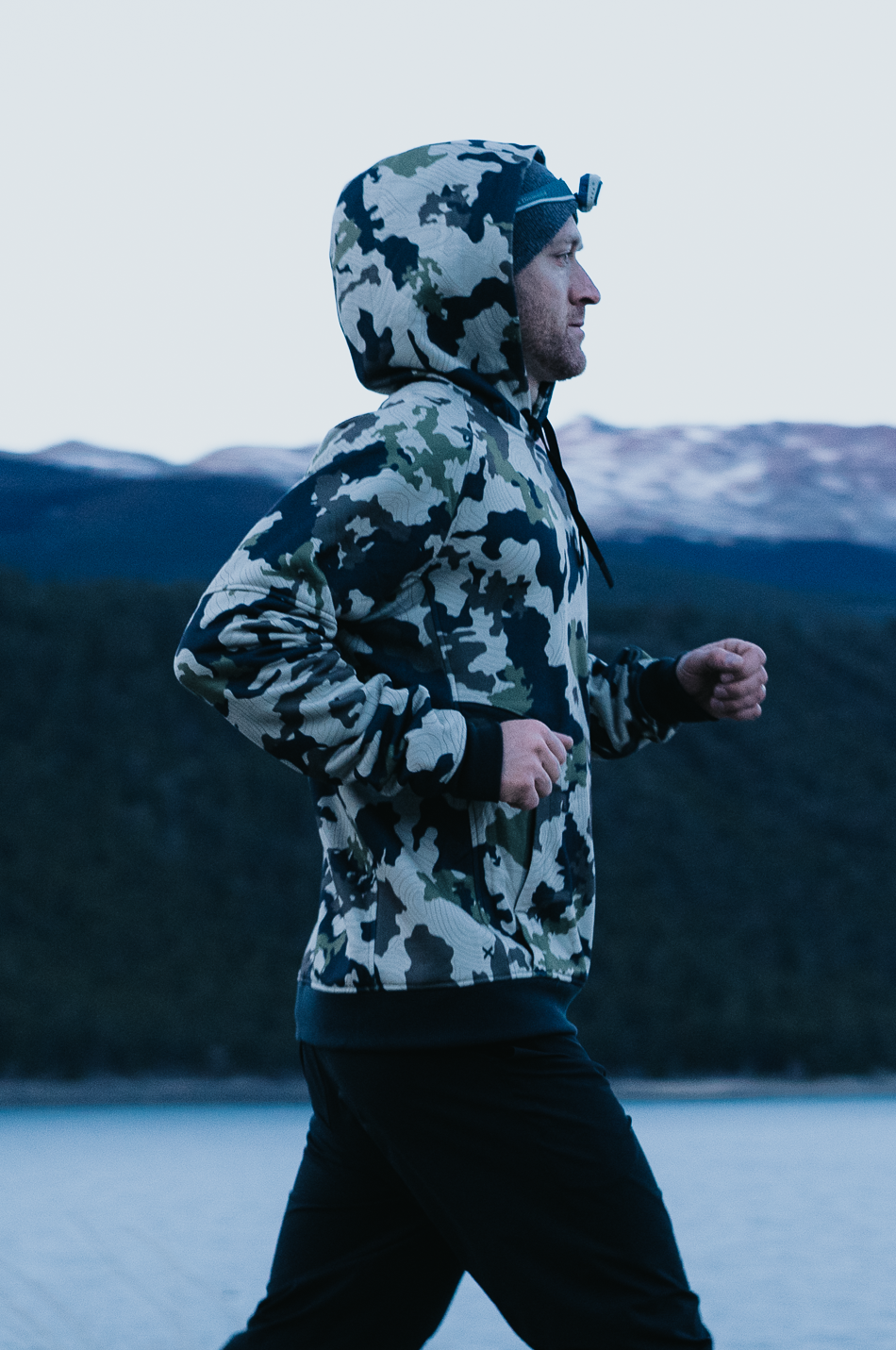 Person wearing a camouflage jacket running in a mountainous landscape
